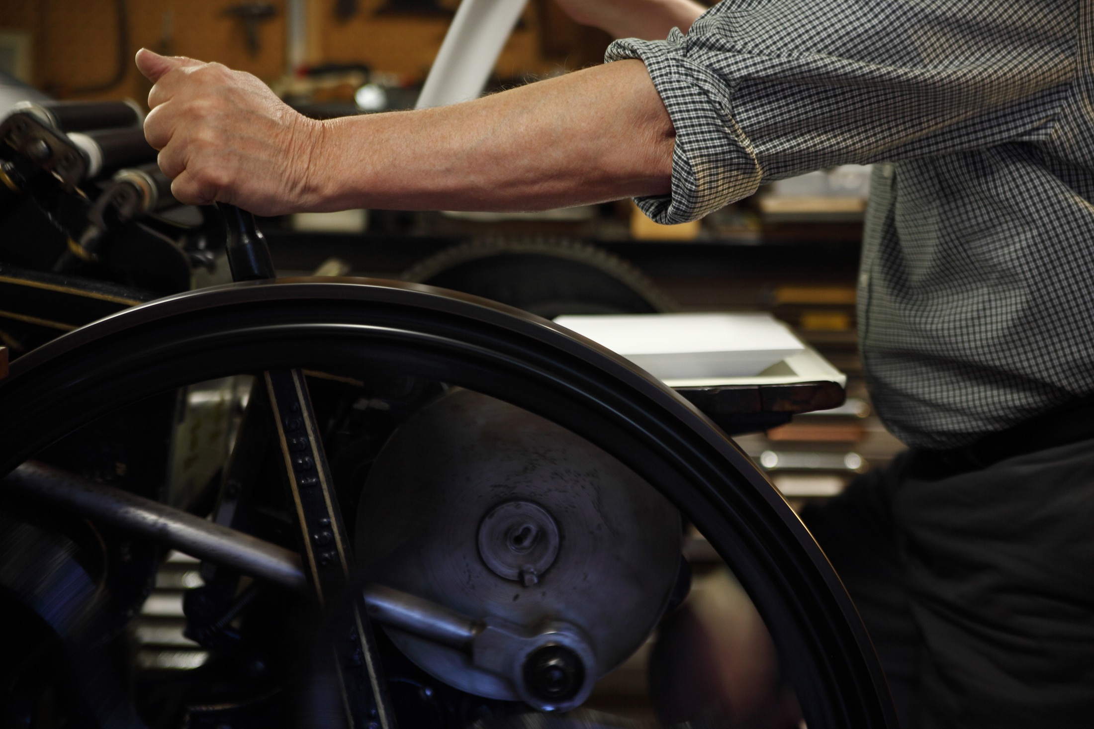 A press operator turning the flywheel of a vintage letterpress